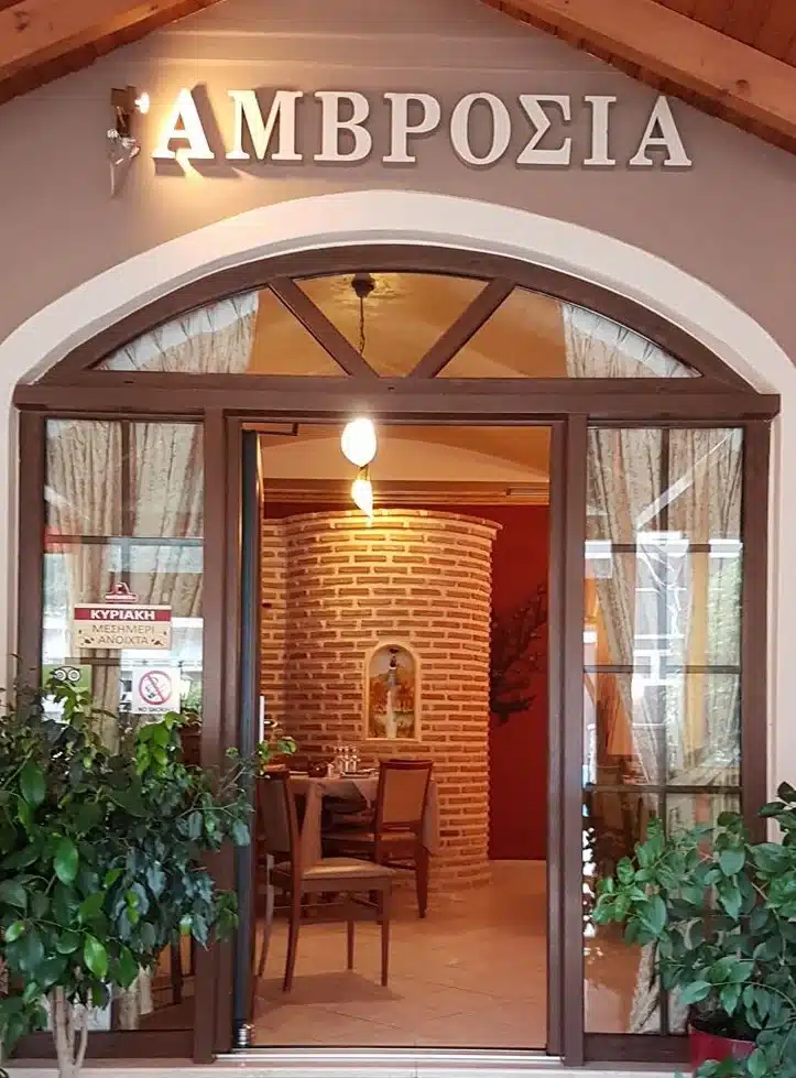Arched entrance of Ambrosia restaurant with its sign in Greek lettering and potted plants