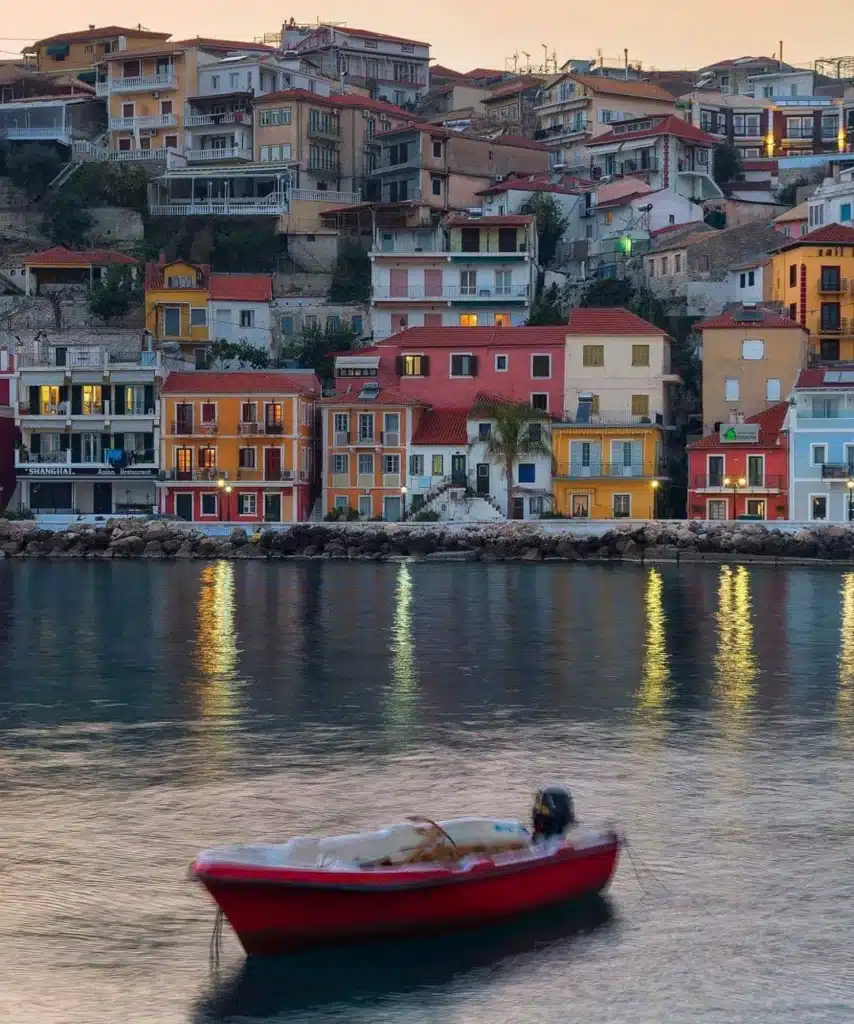 Colorful waterfront houses reflected in calm water, with a red boat on the sea