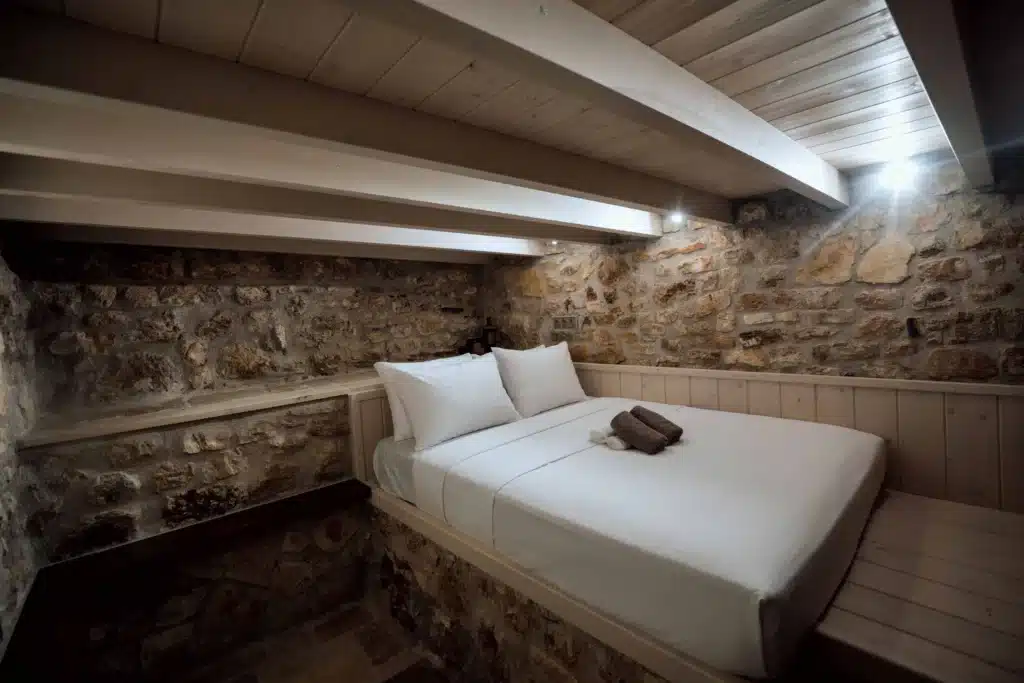 Bright bedroom with a double bed, white beamed ceiling and a stone wall, Valaes Guesthouse, Foiniki