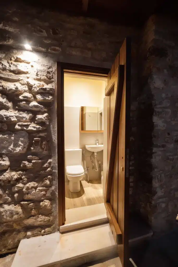 En-suite bathroom with a stone wall, toilet and washbasin, Valaes Guesthouse, Foiniki