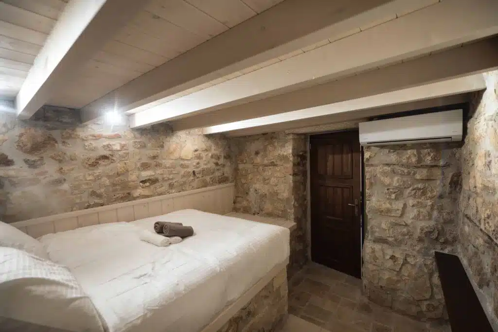 Stone-walled bedroom with a double bed and beamed ceiling, Valaes Guesthouse, Foiniki