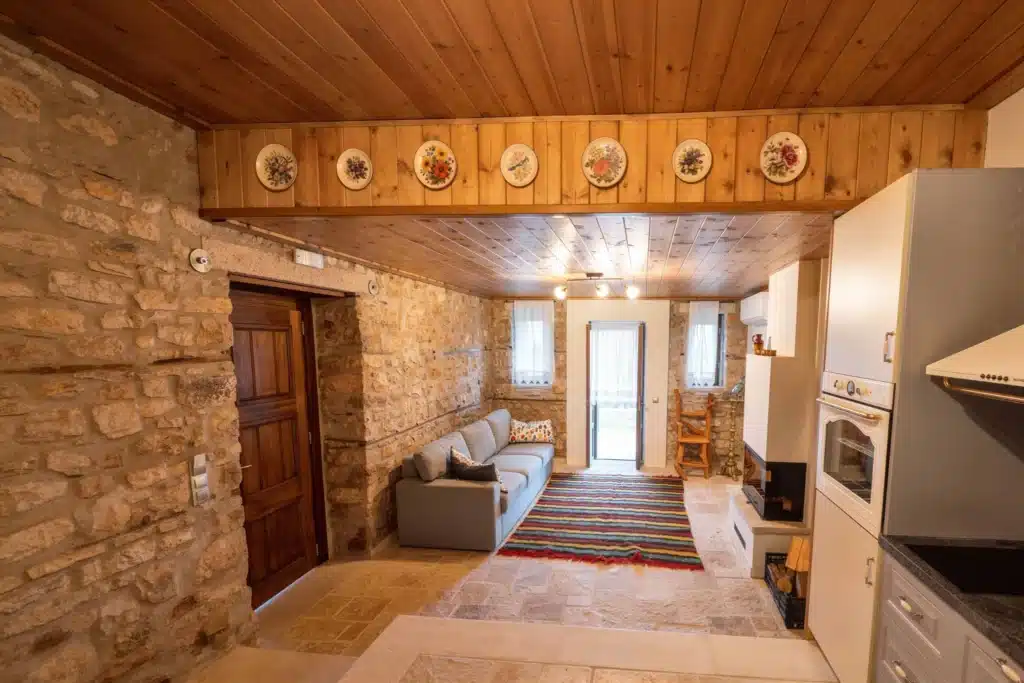 Stone-walled living room with a wooden door and a colourful striped rug, Valaes Guesthouse, Foiniki