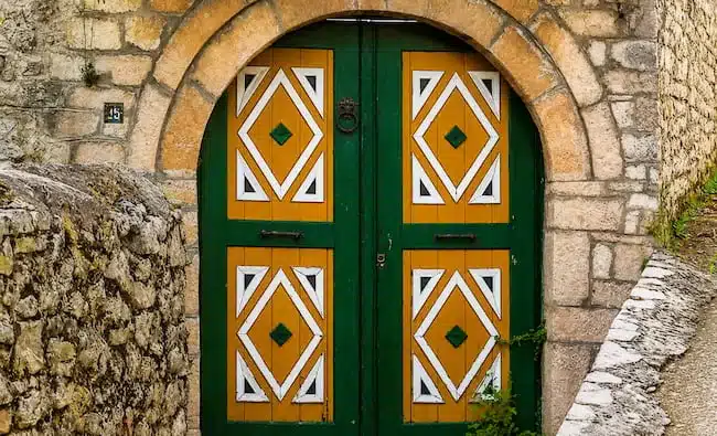 Green wooden double door with diamond-shaped yellow panels in a stone arch