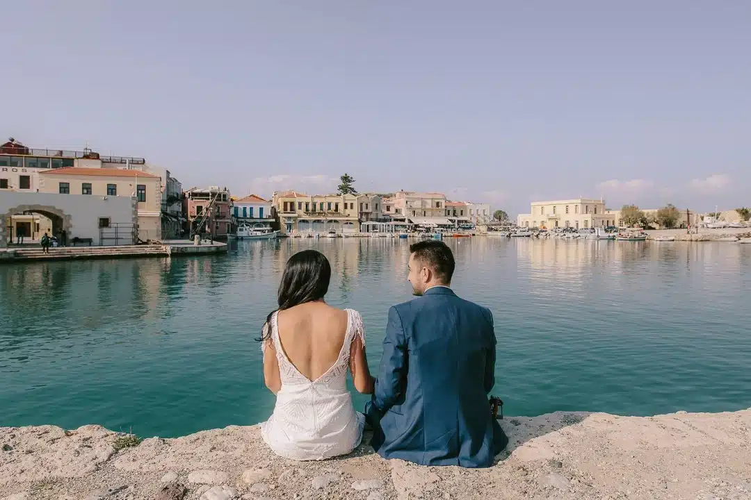 Ζευγάρι νεόνυμφων καθισμένο σε βράχια με θέα μια πόλη-λιμάνι απέναντι, Define Art